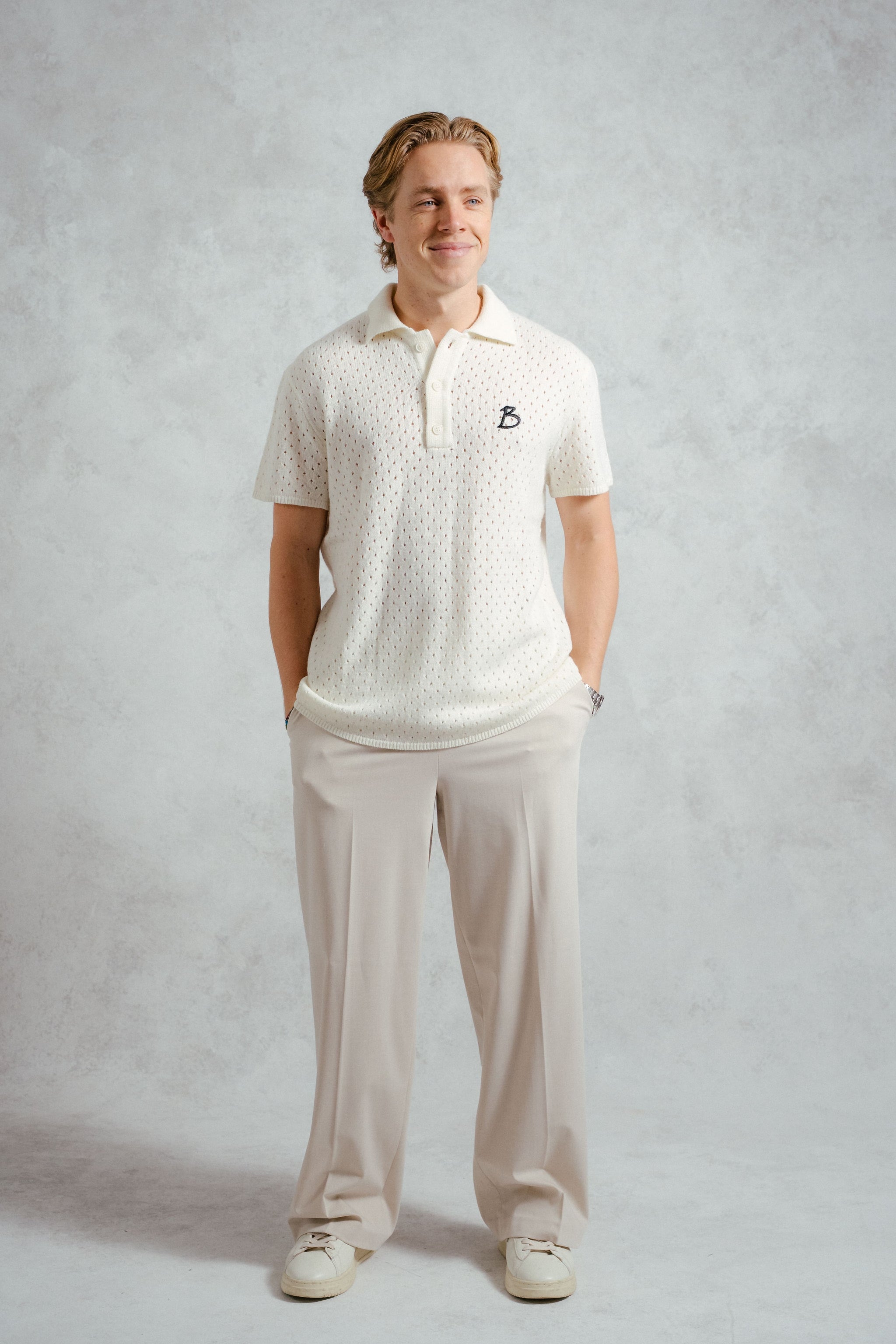 Man wearing a white polo shirt and pants on a plain background