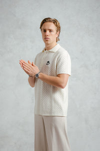 Man wearing a white patterned polo shirt with a logo on a gray background