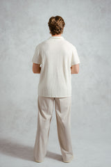 Person wearing a white textured shirt and beige pants against a plain background