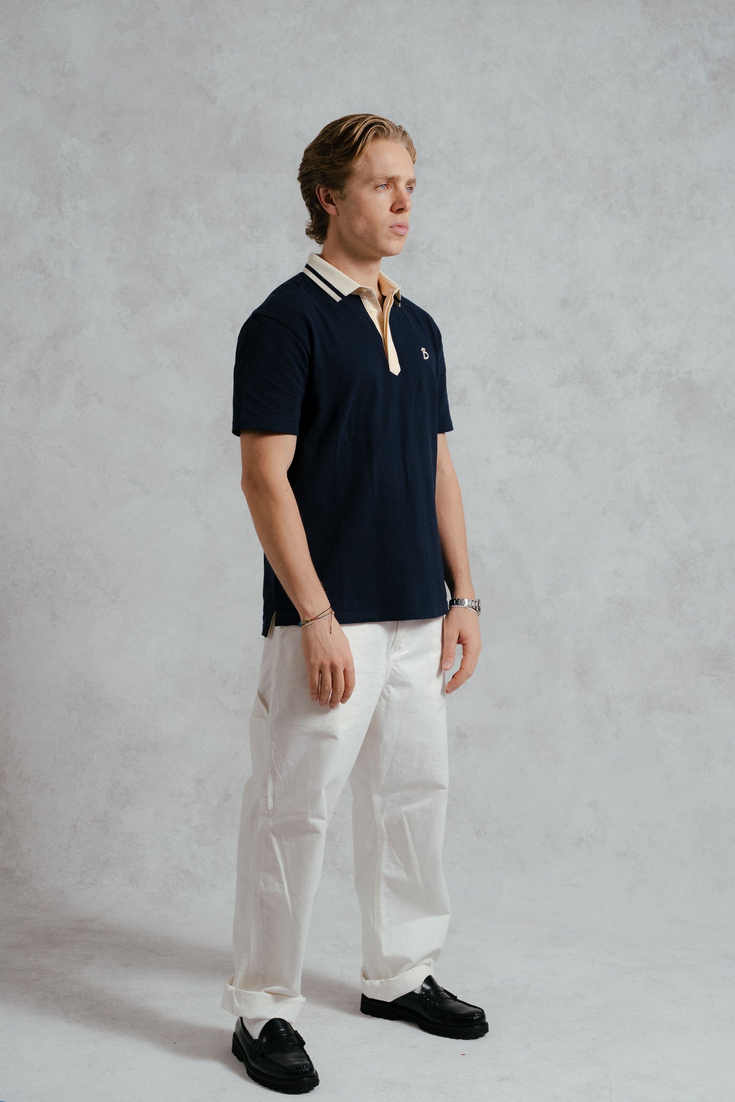 Man wearing a navy polo shirt and white pants against a gray background