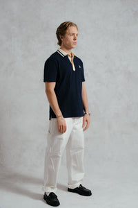 Man wearing a navy polo shirt and white pants against a gray background