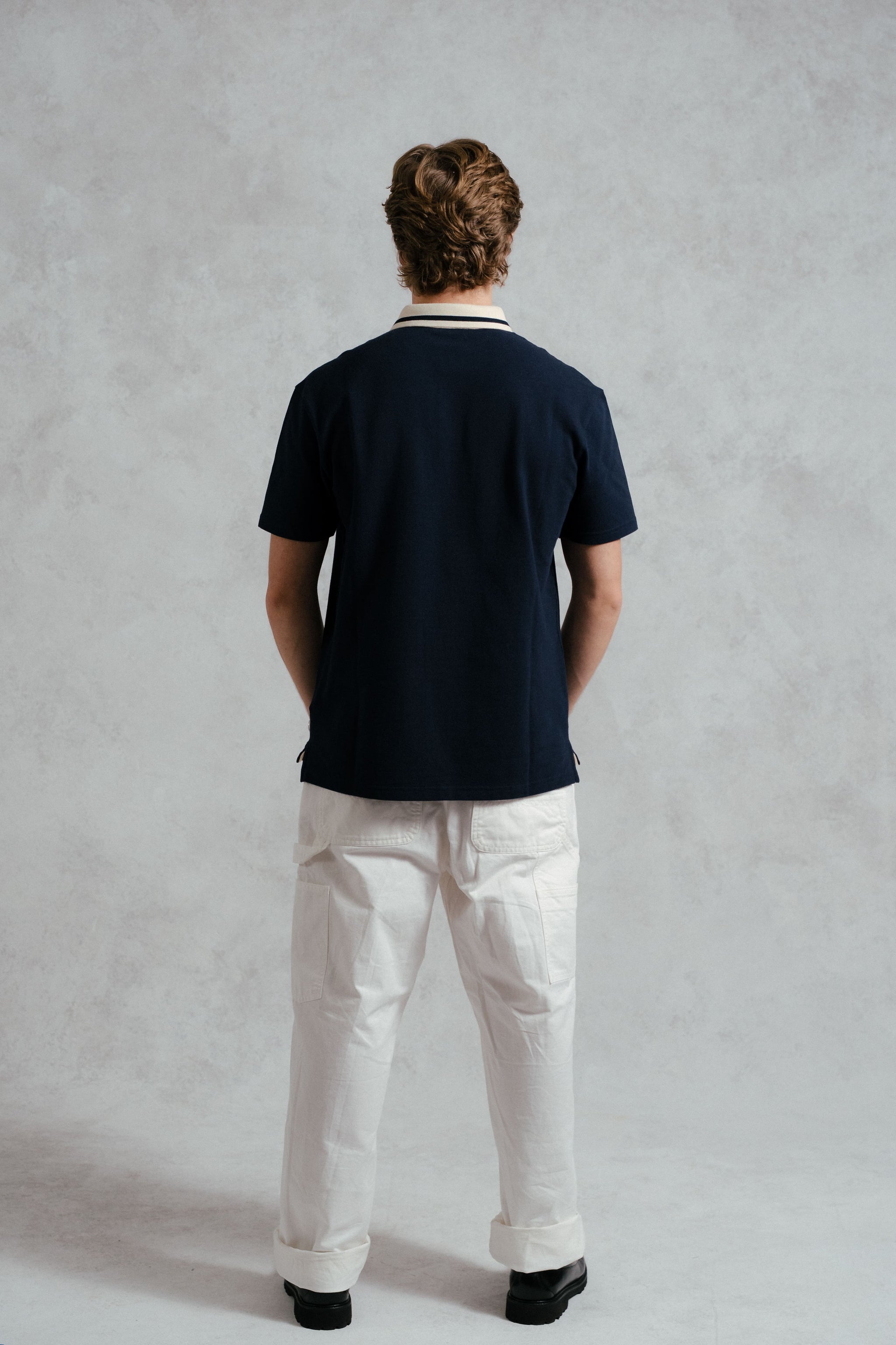 Person wearing a navy polo shirt and white pants against a plain background