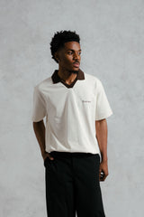 Man wearing a white polo shirt with a collar and black pants against a gray background