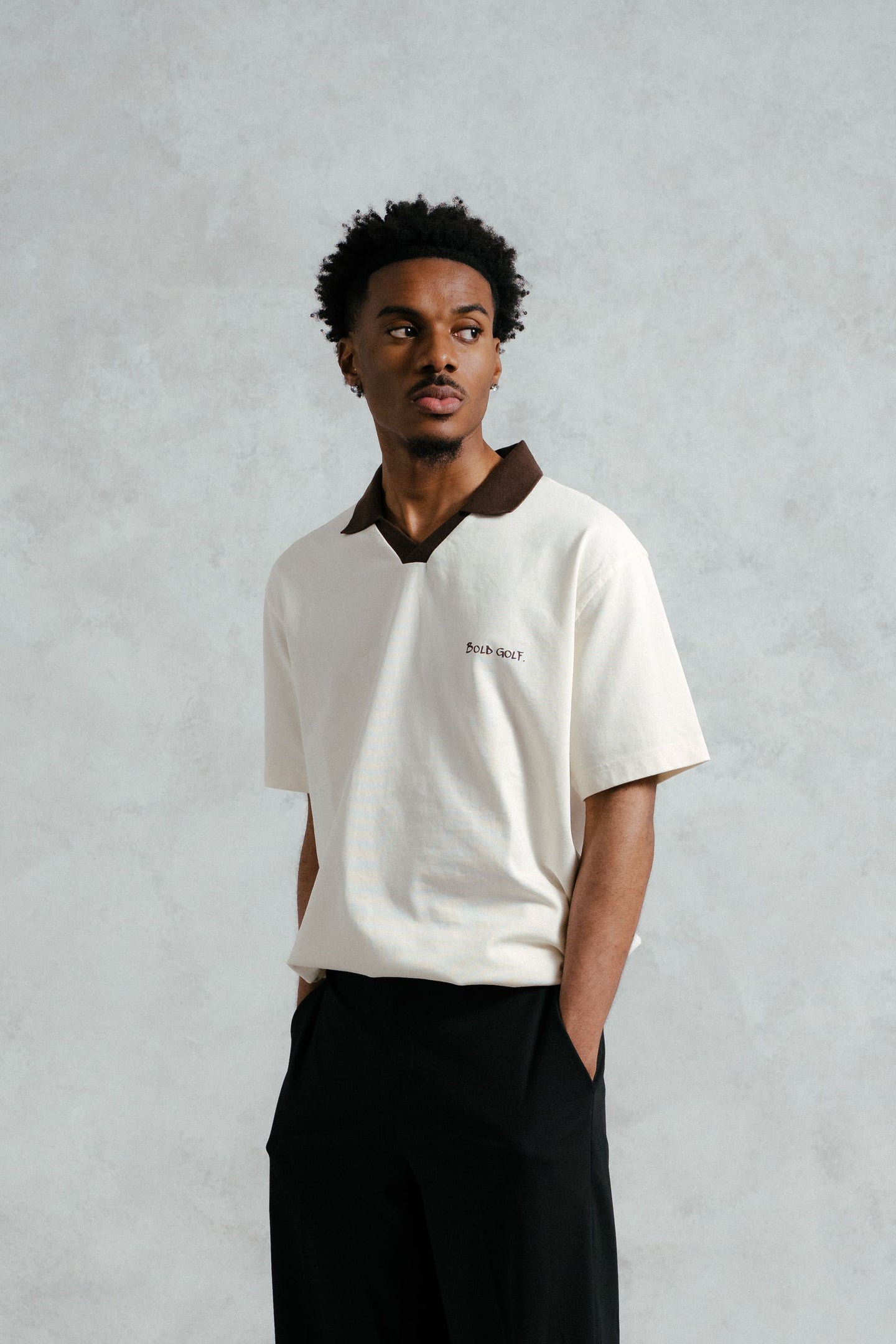 Man wearing a white polo shirt with a brown collar against a gray background