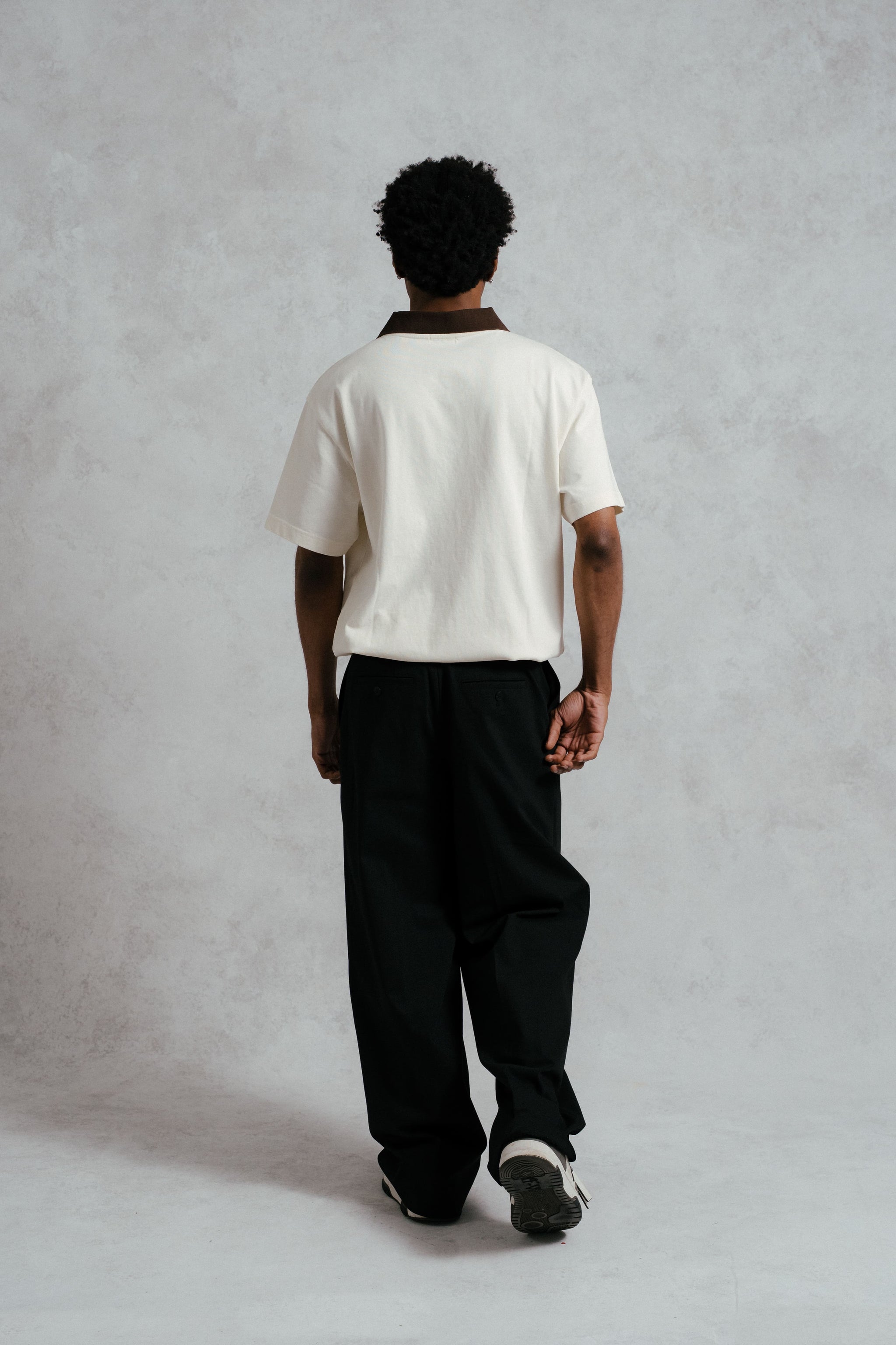 Person wearing a white shirt and black pants against a plain background