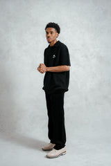 Man wearing a black polo shirt and pants on a light gray background