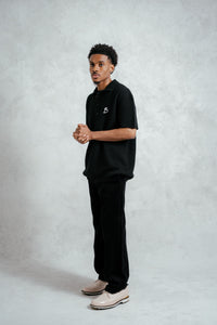 Man wearing a black polo shirt and pants on a light gray background