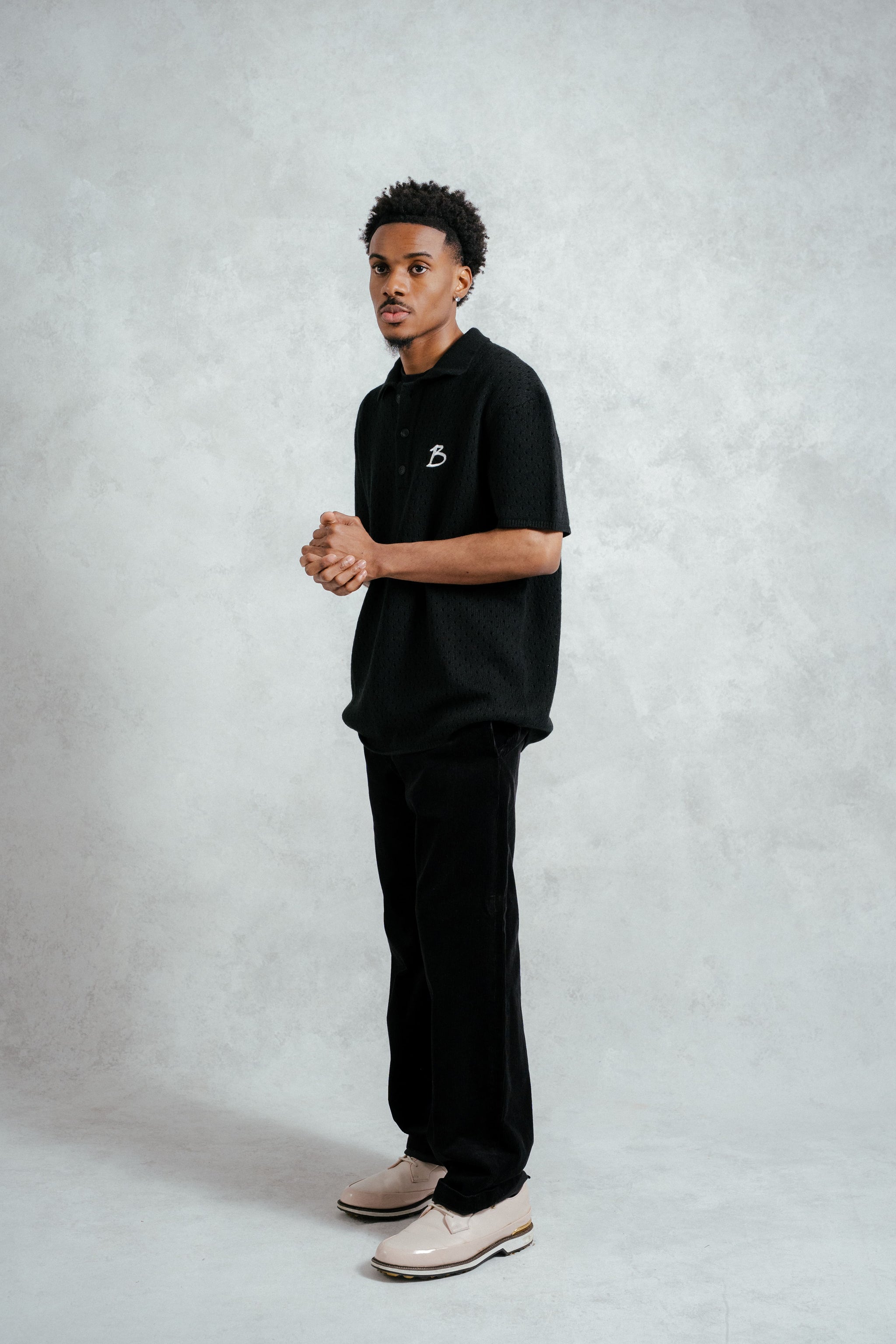 Man wearing a black polo shirt and pants on a light gray background