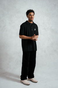 Person wearing a black polo shirt with a logo on a gray background