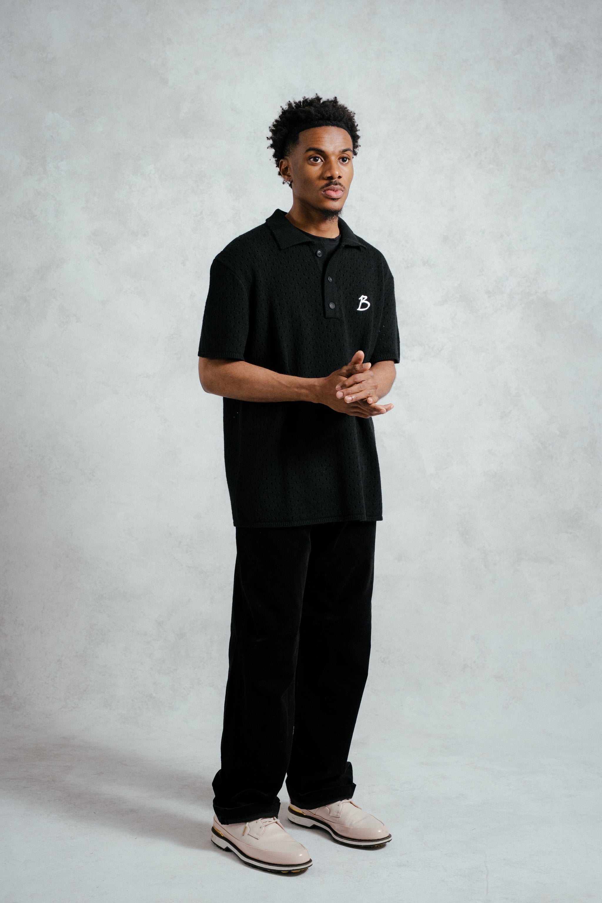 Person wearing a black polo shirt with a logo on a gray background