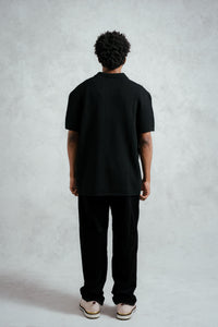 Person wearing a black polo shirt and pants against a plain background