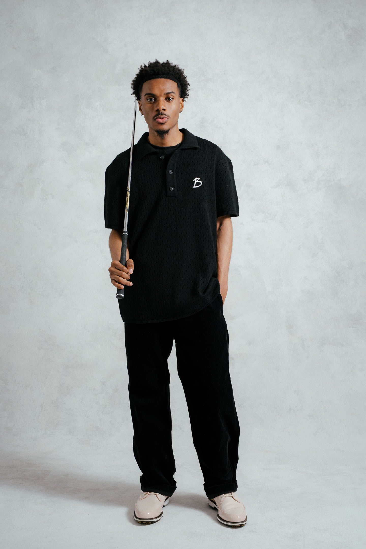 Person wearing a black polo shirt with a logo, holding a fishing rod on a gray background