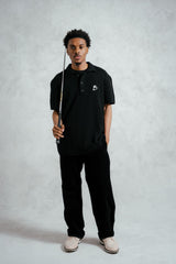 Person wearing a black polo shirt with a logo, holding a fishing rod on a gray background